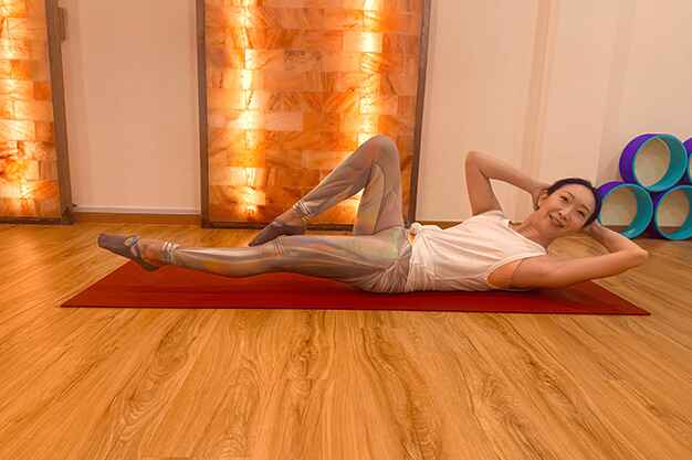 A Pilates instructor demonstrating an oblique twist exercise during a core-strengthening Pilates class at Sky Yoga studio in Tanjong Katong, Singapore.